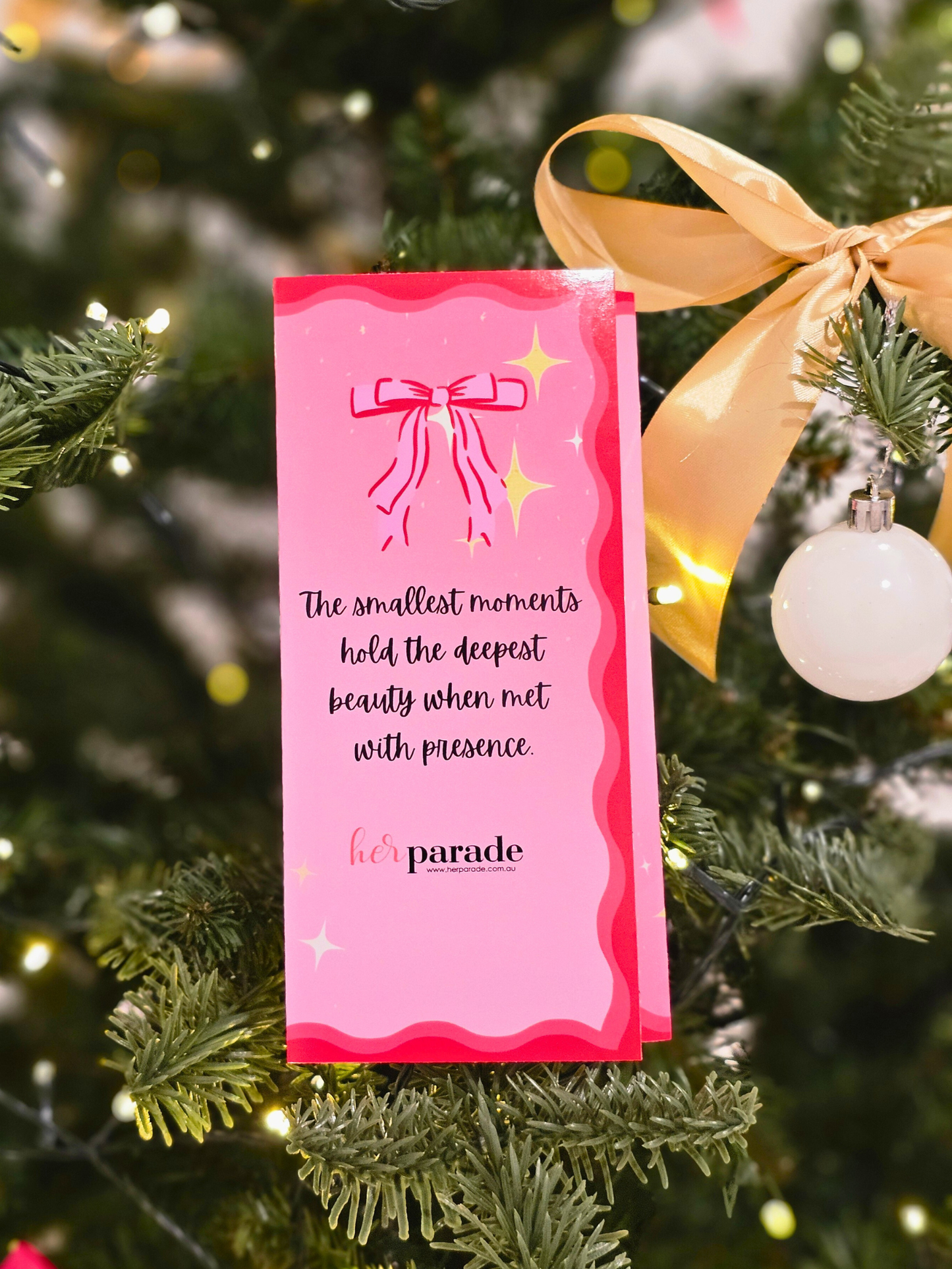 Pink card with motivational design with text and a bow design, attached to a Christmas tree with ornaments.