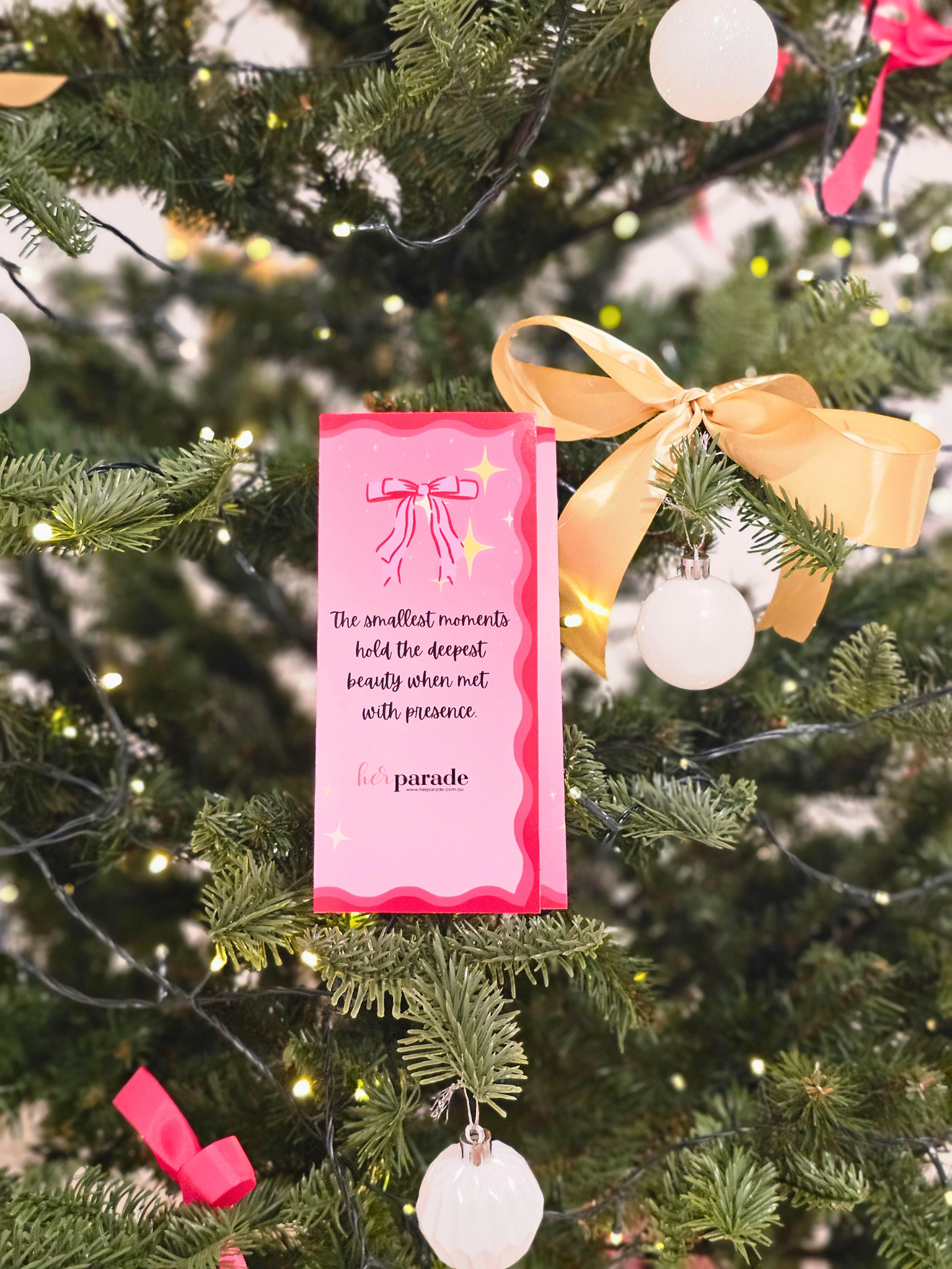 Pink book or card with text on a Christmas tree with ornaments and lights.